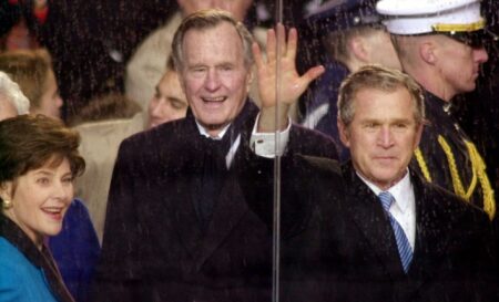 FILE - In this Jan. 20, 2001, file photo, standing in the rain, President George W. Bush waves as he watches his inaugural parade pass by the White House viewing stand in Washington, Saturday afternoon, Jan. 20, 2001.  With him are his wife and first lady Laura Bush and his father,  former President George H.W. Bush. The inauguration of the U.S. president is traditionally a highly-scripted celebration, with seating charts, schedules, dress rehearsals, and planning committees that map each moment of the history-making day from start to finish. But sometimes the unexpected happens. The last time the nation had seen a president's father live long enough to attend his son's inauguration was 40 years earlier, when Joseph Kennedy watched the inauguration of President John F. Kennedy in 1961. (AP Photo/Stephan Savoia)