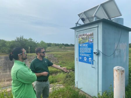 Roberto Vega (left) and Jonathan Holley with the Harris County Flood Control District stand in front of a water quality monitoring station at the Willow Springs Regional Stormwater Detention Basin in Deer Park.