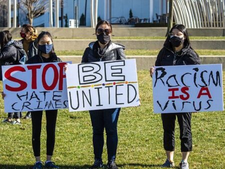 three people hold handwritten signs that say "stop hate crimes, be united, racism is a virus"