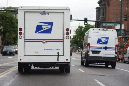 FILE - A USPS logo adorns the back doors of United States Postal Service delivery vehicles as they proceed westbound along 20th Street from Stout Street and the main post office in downtown Denver, Wednesday, June 1, 2022. USPS plans to substantially increase the number of electric-powered vehicles it’s buying to replace its fleet of aging delivery trucks, officials said Wednesday, July 20, 2022. (AP Photo/David Zalubowski, File)