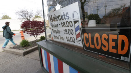 FILE - In this May 6, 2020 file photo, a woman walks past a closed barber shop in Cleveland. Small businesses are in limbo again as the coronavirus outbreak rages and the government’s $659 billion relief program draws to a close. Companies still struggling with sharply reduced revenue are wondering if Congress will give them a second chance at the Paycheck Protection Program, which ends Friday, Aug. 7,  after giving out 5.1 million loans worth $523 billion.  (AP Photo/Tony Dejak, File)
