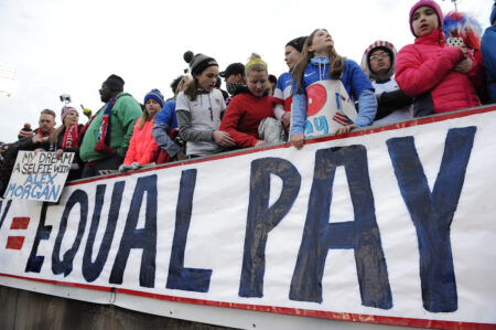 FILE - In this April 6, 2016, file photo, fans stand behind a large sign for equal pay for the women's soccer team during an international friendly soccer match between the United States and Colombia at Pratt & Whitney Stadium at Rentschler Field in East Hartford, Conn. The U.S. Soccer Federation and the World Cup champion women's team have agreed on a labor contract, settling a dispute in which the players sought equitable wages to their male counterparts. The financial terms and length of the multiyear deal were not disclosed. The agreement was ratified by the players and the federation's board Tuesday, April 4, 2017.