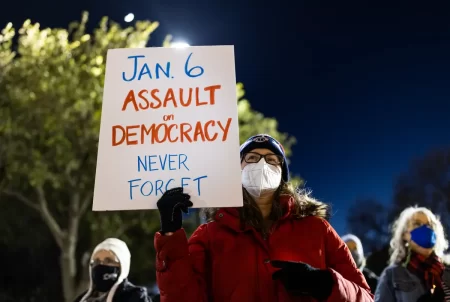A woman holds a sign at a candlelight vigil at the Texas Capitol on Jan. 6, 2022, to mourn the one-year anniversary of the attack on the U.S. Capitol.