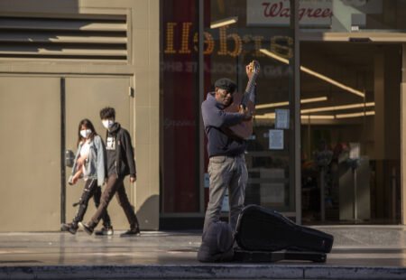 A lone street performer tunes his guitar on a mostly-empty Hollywood Boulevard in Los Angeles, Tuesday, March 24, 2020.