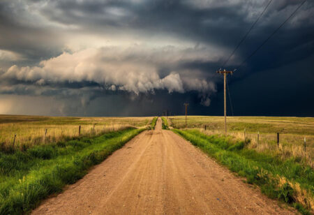 A dirt road with a storm cloud in the distance.