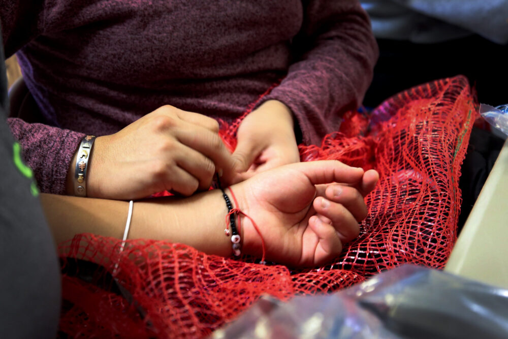 A migrant seeking asylum helps another put on a bracelet once they receive their personal effects back after arriving at Oak Lawn United Methodist Church in Dallas. The church will feed, clothe and transport the migrants to the next leg of their journey.