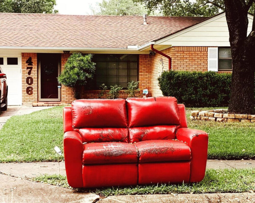 A red loveseat on a curb in front of a Houston house