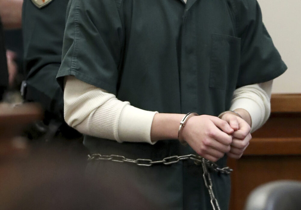 A closeup of a man's hands in handcuffs and chains entering a courtroom