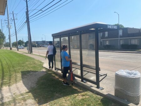 Metro bus riders seek shade in the shadow cast behind the bus shelter.
