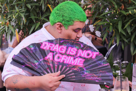 Attendee at ReBar's drag brunch accessorizes with a neon fan that says "DRAG IS NOT A CRIME"