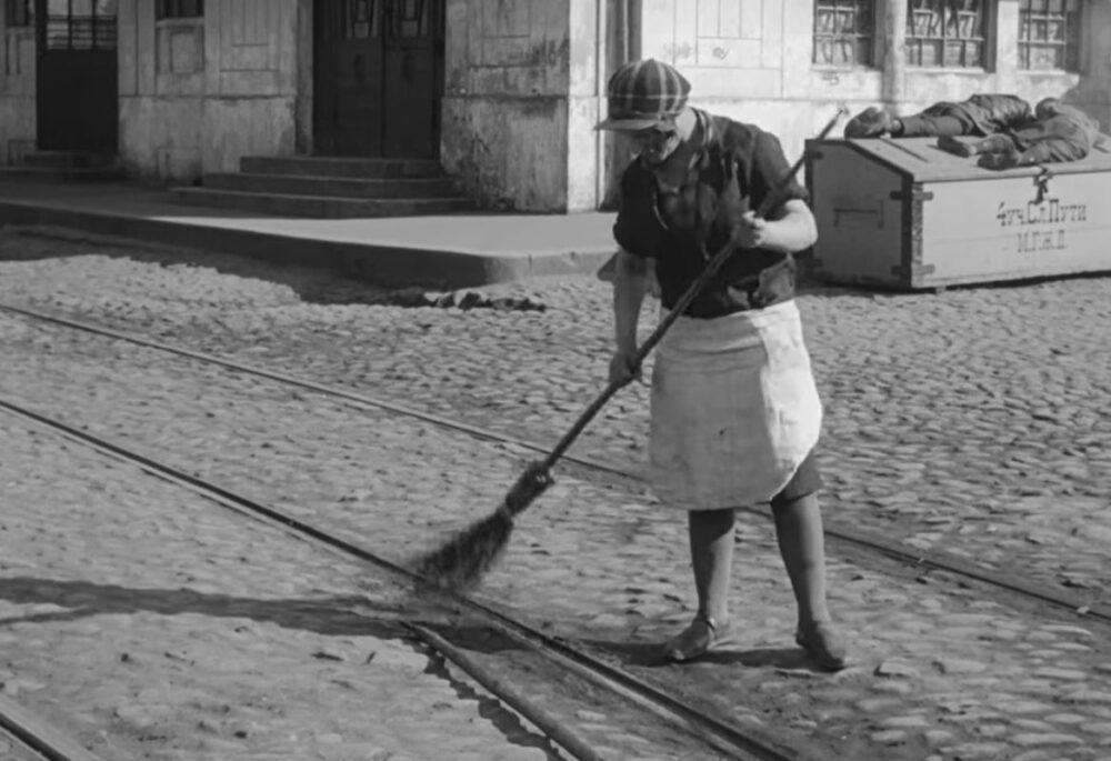 A black and white image of a Russian woman sweeping a street