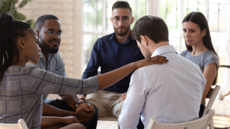 Rear view at upset man feel pain depression problem addiction get psychological support of counselor therapist coach diverse people friend group help patient during therapy counseling session concept.