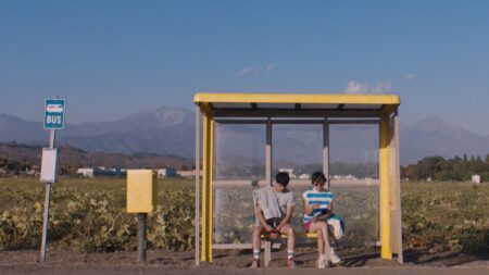 Still from film of two boys waiting outside at a bus stop