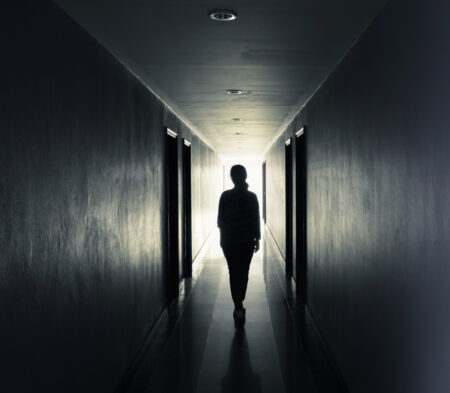 A girl walks in a dark hotel hallway.