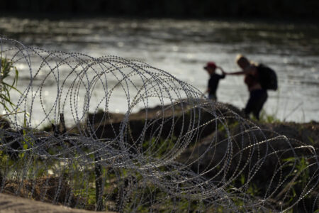 Migrants in Eagle Pass, Texas walk near concertina wire erected by state officers participating in Operation Lone Star.