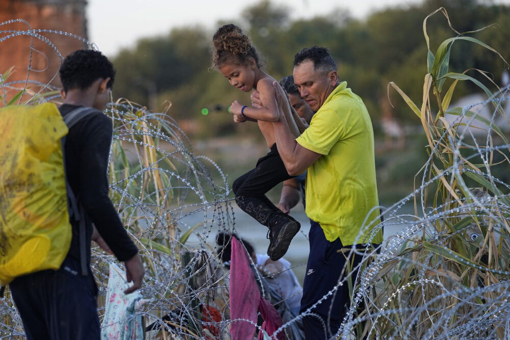 A young girl is lifted over concertina wire are she and other other migrants crossed the Rio Grande and entered the U.S. from Mexico head to be processed by U.S. Customs and Border Protection, Saturday, Sept. 23, 2023, in Eagle Pass, Texas. (AP Photo/Eric Gay)