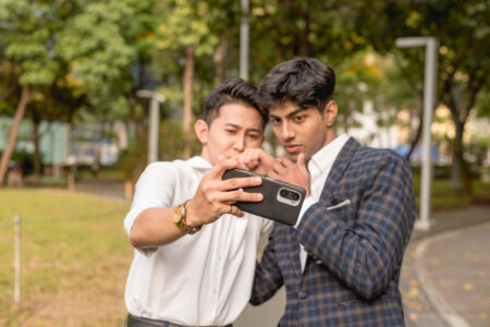 Two young asian men watch a controversial or shocking video on their cellphone. During break time at the office.