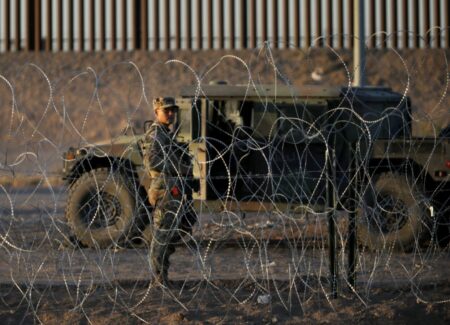 FILE PHOTO: A Texas National Guard Soldier watches for migrants looking to cross the Rio Grande in El Paso behind miles of laid out concertina wire.
