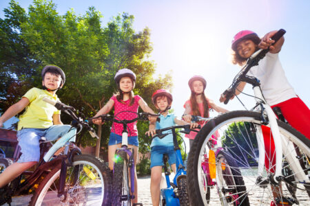 Group of multiethnic children in safety helmets, standing with their bicycles in summer park