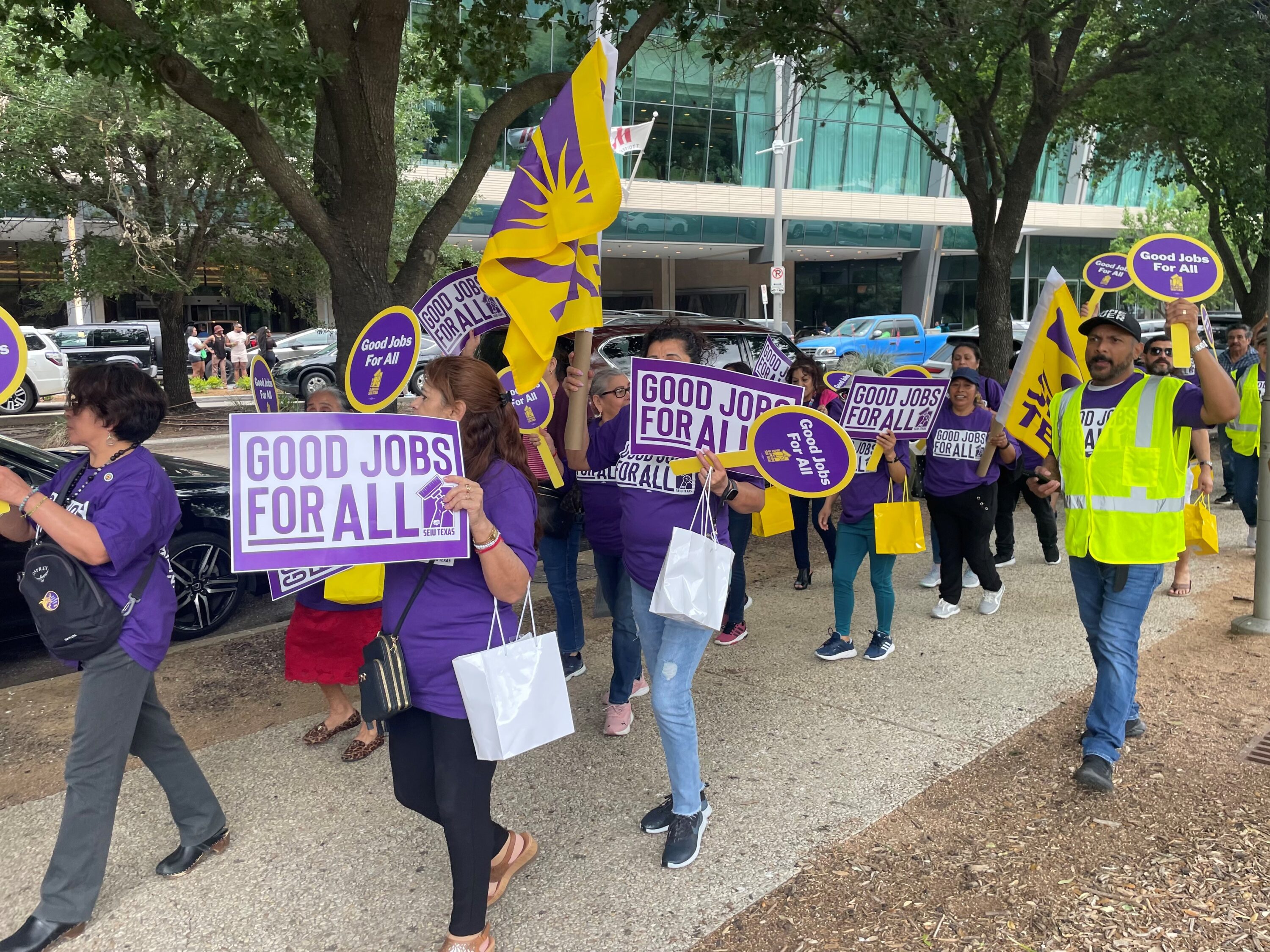 Members of the Service Employees International Union in Houston march downtown in support of higher wages for janitorial workers. They are wearing purple and holding signs that read "Good jobs for all!"