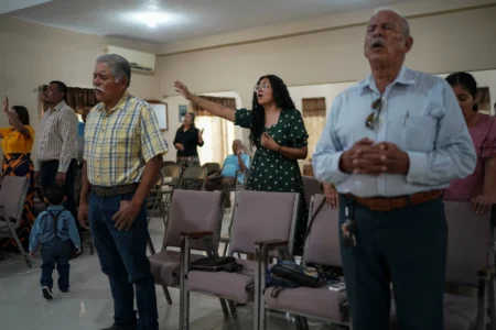 Claudia Gonzalez wears a green dress and raises her hands in worship at a church