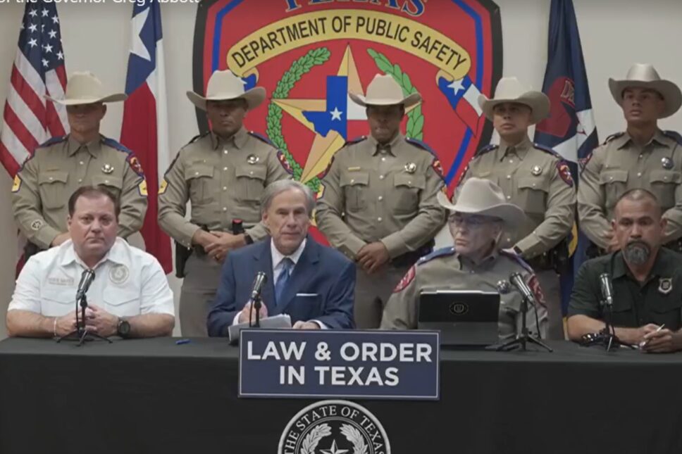 Governor Greg Abbott is surrounded by police officers as he sits at a table.