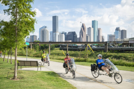 People ride bikes with the downtown Houston skyline in the background