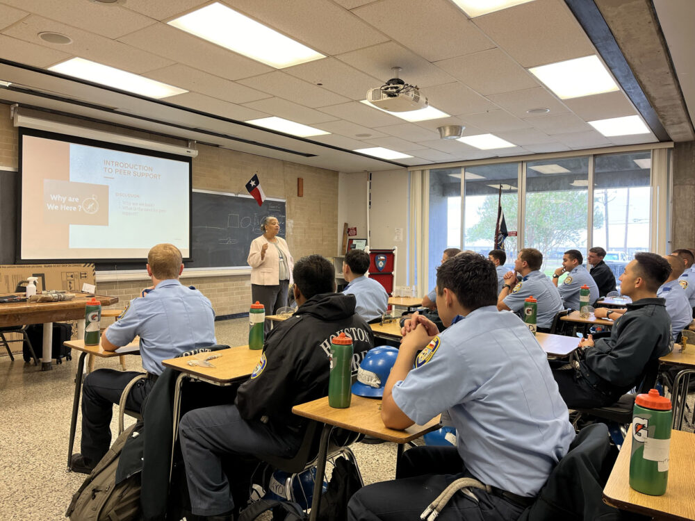 Houston fire cadets listening to a woman at the front of a classroom.