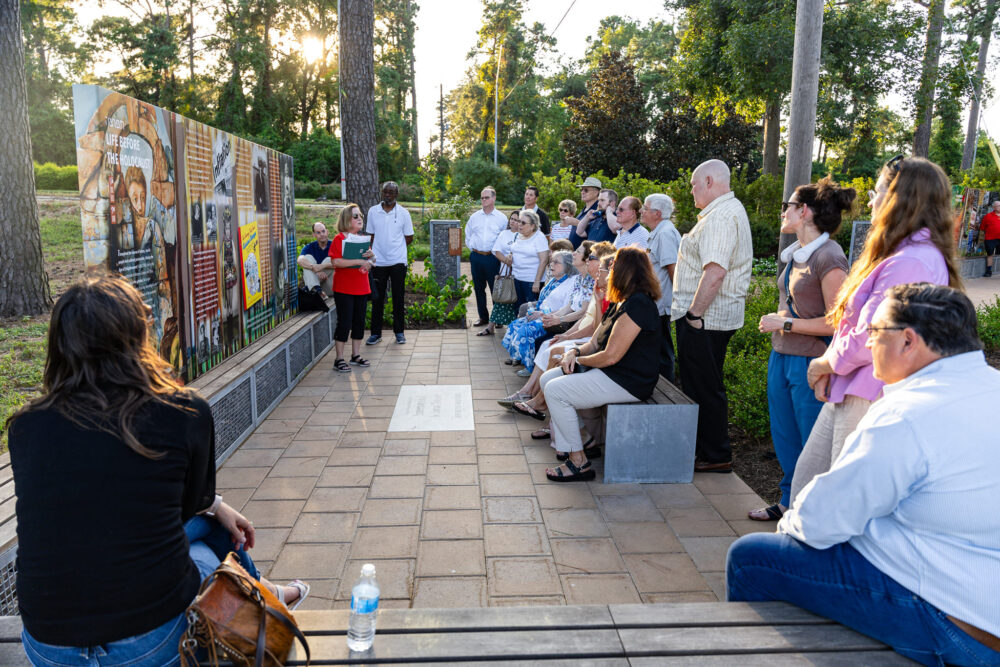 A group of people listen as a tour guide talks about memorials 