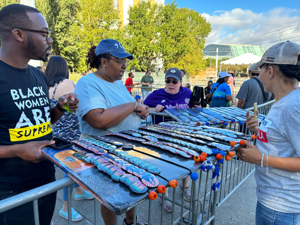 Participants hand out Harris buttons and hats to those in line for Friday's rally. (Image credit: Lucio Vasquez / HPM)