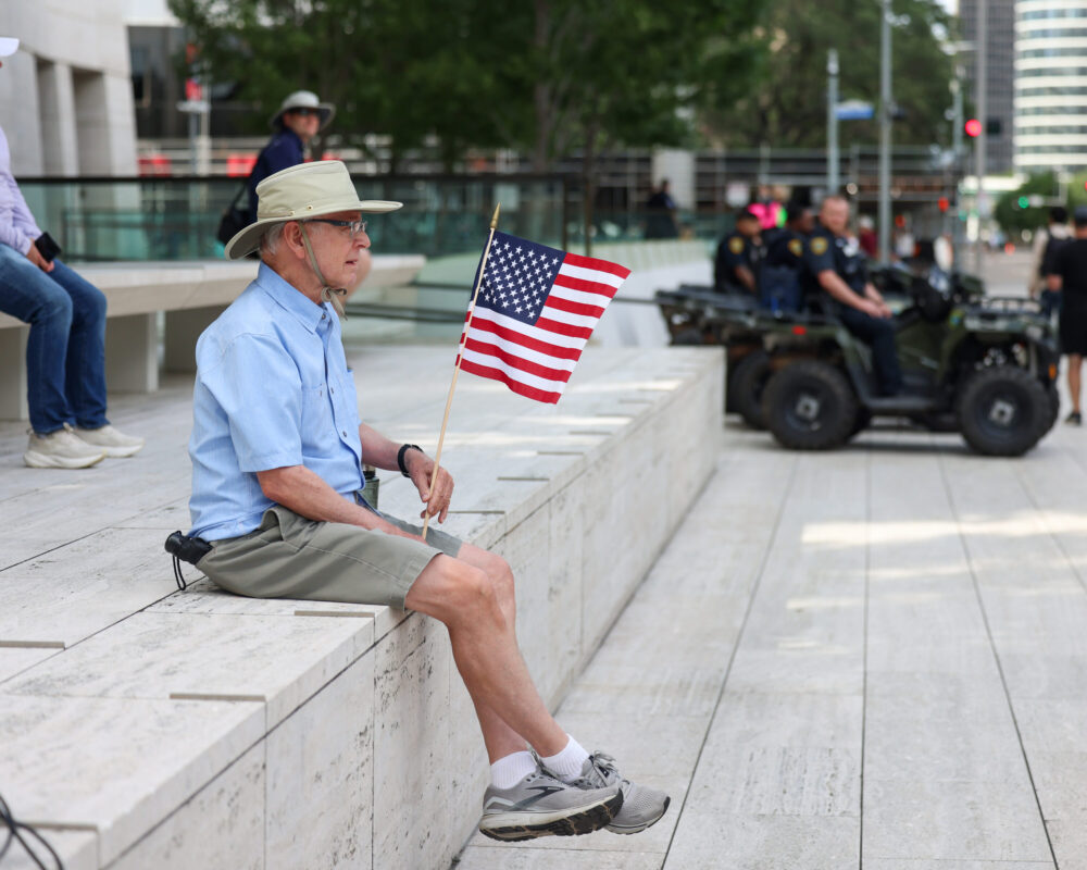 Seorang pria yang memiliki bendera Amerika berada dalam langkah di luar kota Houston pada hari Sabtu, 14 Juni 2025. (Kredit foto: Rob Salinas/Houston Public Media)