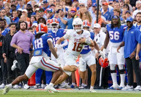 Two football players face off while running on the field, as a crowd watches in the background.