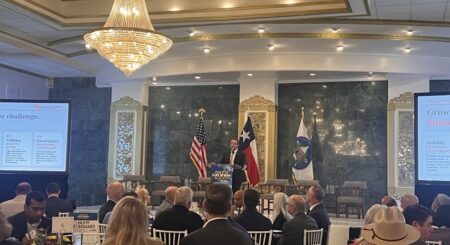 A ballroom filled with people sitting in chairs and a speaker at a podium in front.